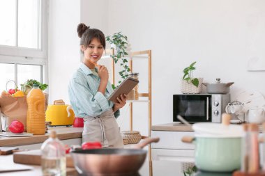 Mutfaktan yiyecek ve defter alan düşünceli genç bir kadın.