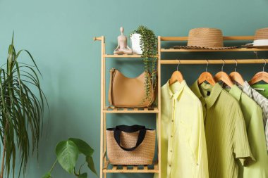 Soyunma odasındaki yeşil duvarın yanında şapka ve çantaların olduğu elbise askısı.