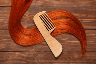 Ahşap arka planda taraklı kızıl saç teli, yakın plan.