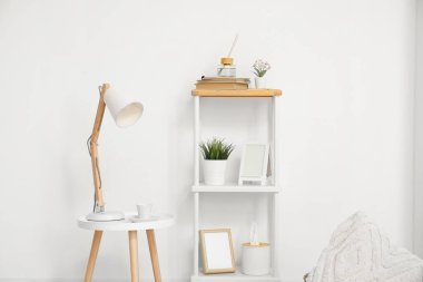 Masa lambası küçük masada ve dekorlu raflar beyaz duvarın yanında.