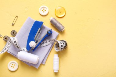 Sarı zemin üzerinde farklı malzemeler bulunan el yapımı dikiş makinesi.