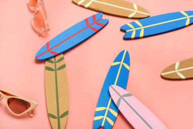 Farklı küçük sörf tahtaları ve pembe arka planda güneş gözlükleri.