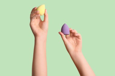 Yeşil arka planda farklı makyaj süngerleri olan kadın elleri