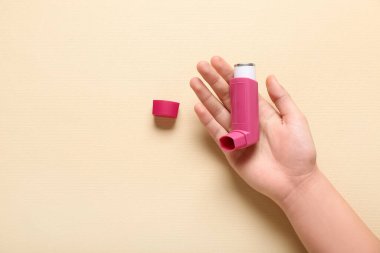 Bej arka planda astım spreyi olan bir çocuk eli.