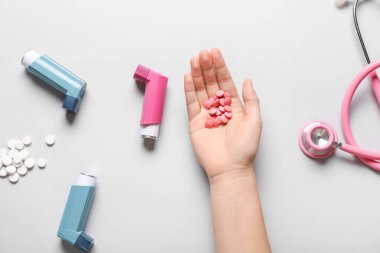 Astım spreyleri, haplar ve beyaz arka planda steteskop ile çocuk eli.