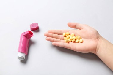 Astım spreyli bir çocuk eli ve beyaz arka planda haplar.