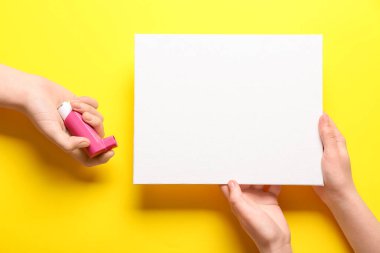 Sarı arka planda astım spreyi ve boş kartla çocuk elleri.