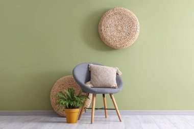 Oturma odasının içinde yeşil duvarın yanında koltuk, yastık ve çiçek var.