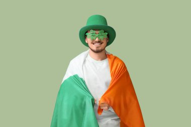 Yeşil arka planda İrlanda bayrağı olan cüce şapkalı mutlu genç adam. Aziz Patrick Günü kutlaması