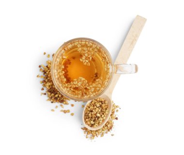 Beyaz arka planda bir bardak taze karabuğday çayı ve tahta kaşık.