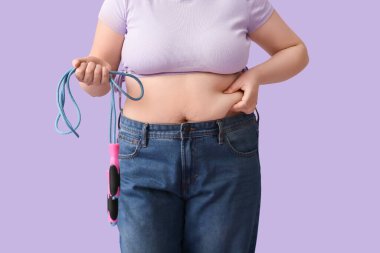 Leylak arka planında ip atlayan şişman bir kadın. Kilo verme konsepti