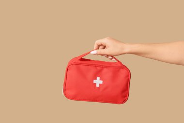 Kahverengi arka planda ilk yardım çantası olan bir kadın.