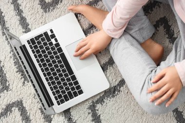 Çıplak ayaklı kadın evdeki halıda dizüstü bilgisayar kullanıyor.