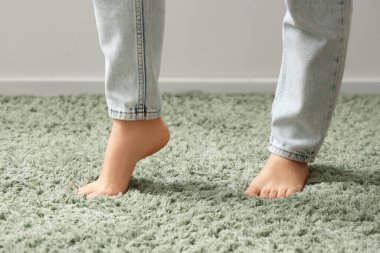 Yeşil tüylü halıda çıplak ayaklı kadın, ışık duvarının yanında, yakın plan.