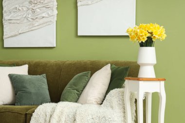 Oturma odasının içinde yeşil kanepe ve masadaki vazolarda nergisler.