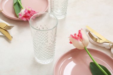 Pembe tabaklar, bardaklar, çatal bıçak takımı ve çiçekli güzel bir masa.