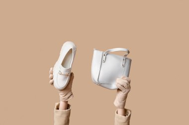 Eldivenli kadın elleri ve bej arka planda çanta ve ayakkabı.