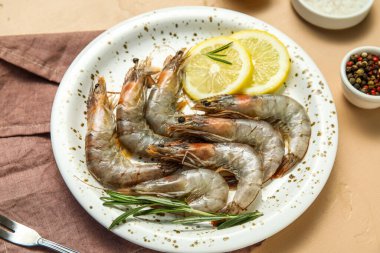 Taze çiğ karidesli tabak, bej arka planda limon ve biberiye