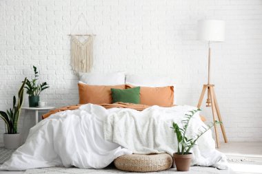 Yatak odasının içinde büyük yatak odası, lamba, sehpa ve bitkiler var.