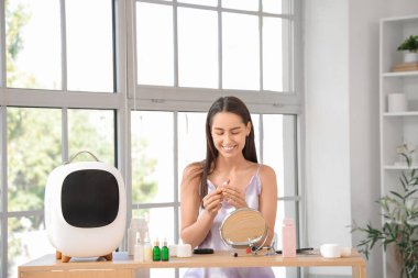 Evde küçük bir buzdolabı ve ruju olan mutlu genç bir kadın var.