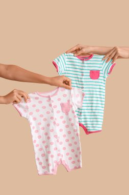 Bej arkaplanda bebek kıyafetleri olan kadın elleri