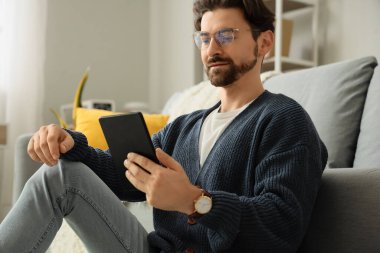 E-okuyuculu genç adam evde oturuyor.