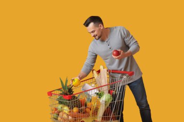 Sarı arka planda alışveriş arabası olan mutlu genç bir adam.