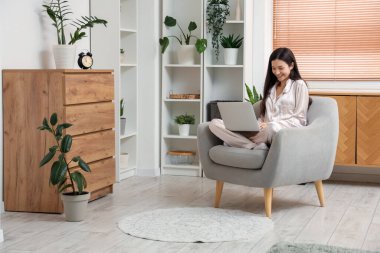 Çizgili pijamalarıyla evde dizüstü bilgisayarla çalışan serbest çalışan bir kadın.