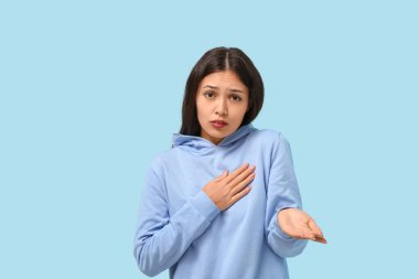 Güzel genç Asyalı özür dileyen kadın mavi arka planda para dileniyor.