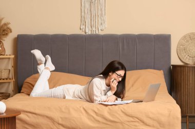 Yatak odasında doküman ve dizüstü bilgisayarla çalışan güzel genç bir kadın.