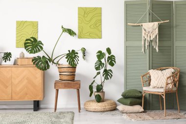 Çekmeceler, katlanan ekran, hasır koltuk ve oturma odasının içindeki Monstera bitkileri.