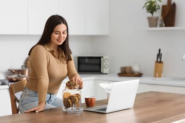 Genç bir kadın mutfakta kavanozdan kurabiye alıyor.