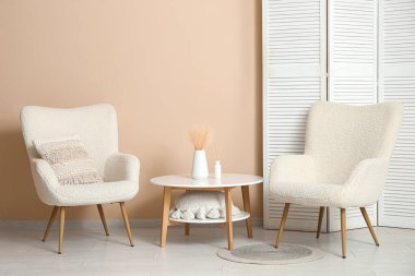 Oturma odasının içinde koltuklar, masa ve bej duvarın yanında katlanan ekran.