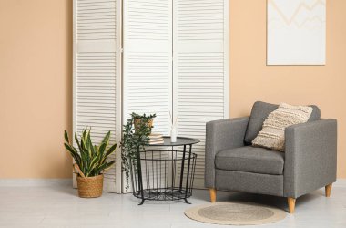 Oturma odasının içinde katlanan ekran, koltuk ve bej duvarın yanındaki masa.