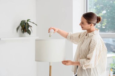 Evde ampulü lambaya sokan genç bir kadın.