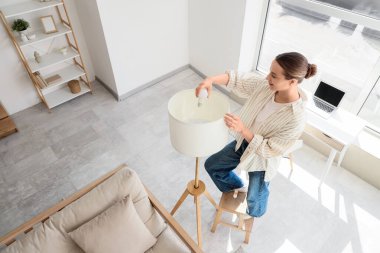 Evde ampulü lambaya sokan genç bir kadın.