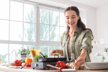 Mutfakta ızgara tavada mısır kızartırken yemek tarifi yazan genç bir kadın.
