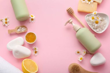 Papatya çiçeğinden yapılmış çerçeve, spa taşları ve pembe arkaplanda kozmetik ürünler, yakın plan