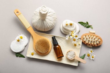 Masaj vücut fırçaları, kozmetik ürünler şişeleri ve gri arka planda papatya çiçekleri olan kompozisyon, yakın plan.