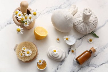 Masaj vücut fırçası, papatya çiçekleri, mermer arka planda kase ve şişe kozmetik ürünleri, yakın plan