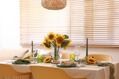 Tabaklar, mumlar ve güzel ayçiçekleri olan zarif bir masa.