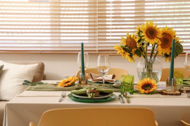 Tabaklar, mumlar ve güzel ayçiçekleri olan zarif bir masa.