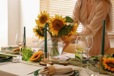 Yemek masasını bir buket güzel ayçiçeğiyle süsleyen genç bir kadın.