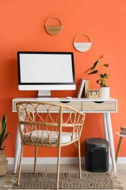 Modern bilgisayar, anthurium çiçeği ve turuncu duvarın yanındaki takvimle rahat çalışma alanı