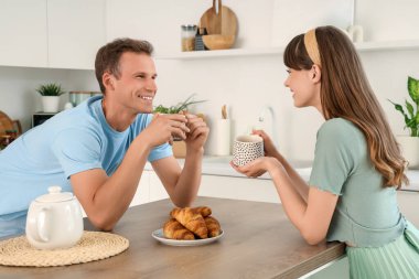 Mutfaktaki masada çay içip kruvasan içen genç bir çift.