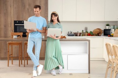 Genç çift mutfakta dizüstü bilgisayar kullanıyor.