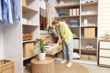 Genç bir kadın gardıroptaki çekmeceden giysilerini alıyor.