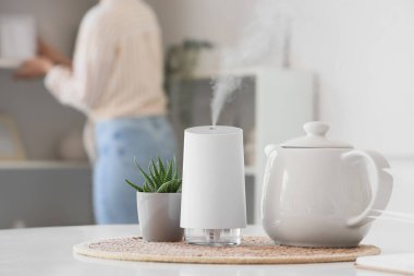 Yemek masasında bitki ve çaydanlık bulunan hava nemlendirici, yakın plan.