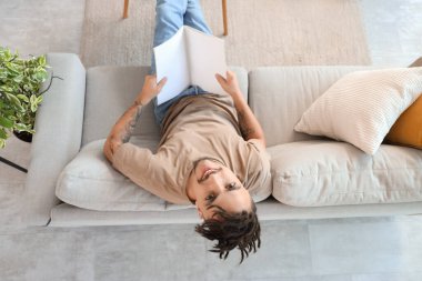 Evdeki kanepede rastalı bir dergi okuyan genç adam.