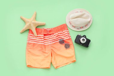 Yeşil arka planda plaj aksesuarları olan çocuk yüzme şortu.